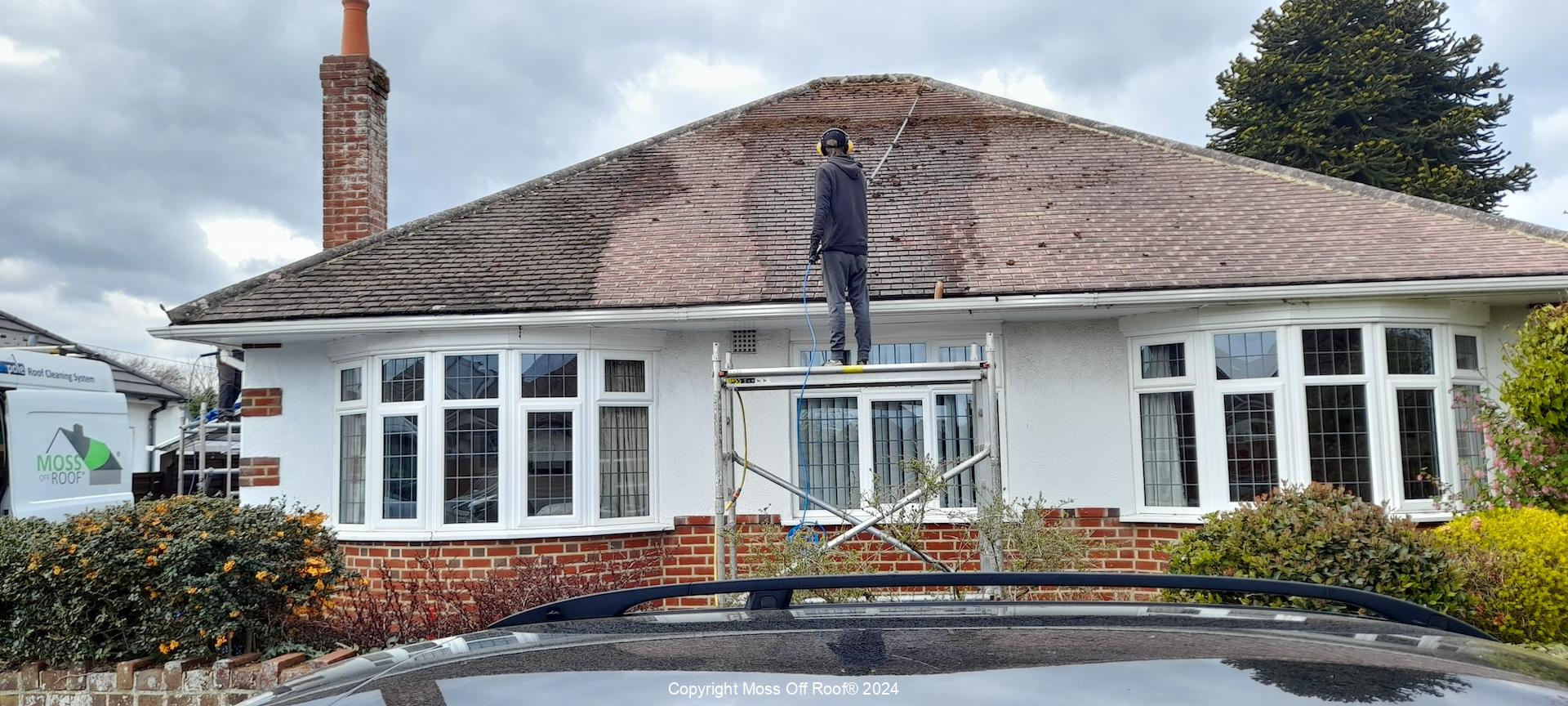 Moss Off Roof technician cleaning rooftop from scaffold platform