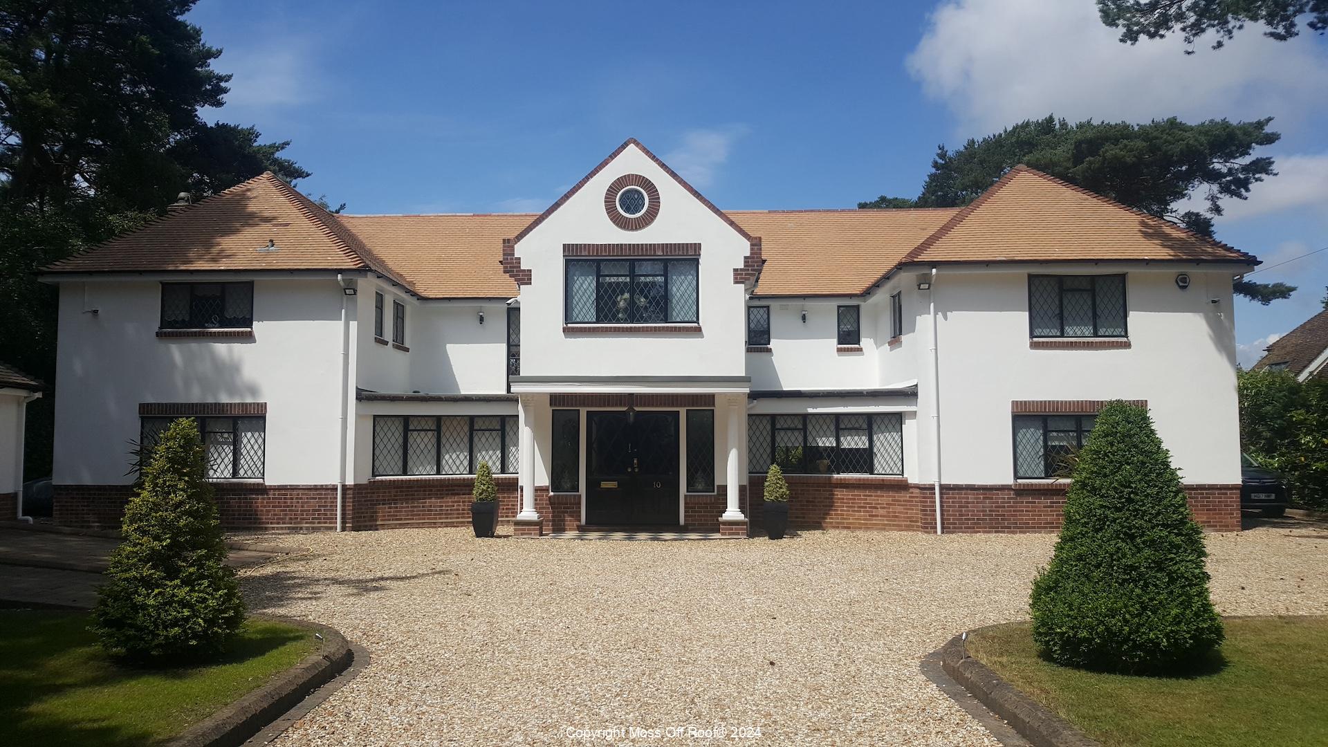 Restored tiled roof on large white detached home after moss removal